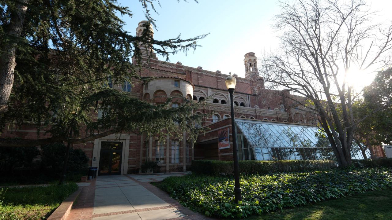 The back entrance of Royce Hall, which features a glass-paned extension and is surrounded by trees.