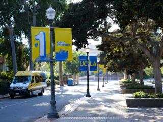 A lamppost-lined street with “#1 Public University” banners, trees, and a parked UCLA van.