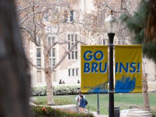 A “Go Bruins!” sign is prominently displayed from a lamppost and two students walk in the background. 